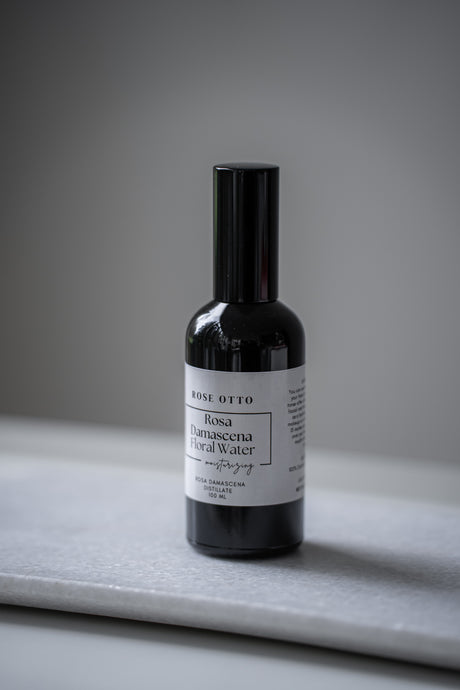 Bottle of Rosa Otto floral water on a gray surface with a neutral background