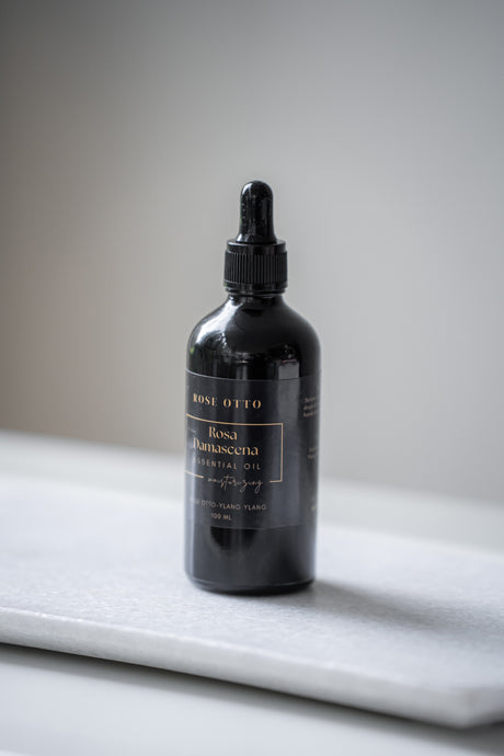 Black dropper bottle labeled 'Rose Otto' on a marble surface with a neutral background