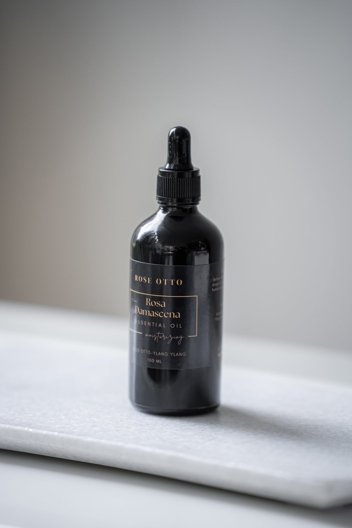 Black dropper bottle labeled 'Rose Otto' on a marble surface with a neutral background